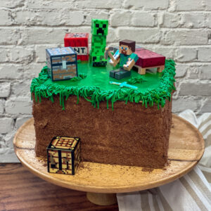 Dětský dort Minecraft ve tvaru grass blocku s postavičkami Creeper a Steve.